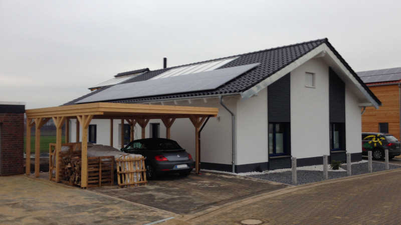 Einfamilienhaus mit Carport und Solarmodulen auf dem Dach in einer Neubausiedlung.