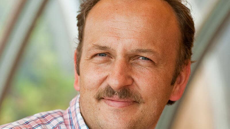 Hubert Becher, Portr&auml;t eines Mannes mittleren Alters mit Schnurrbart im karierten Hemd, leicht l&auml;chelnd.