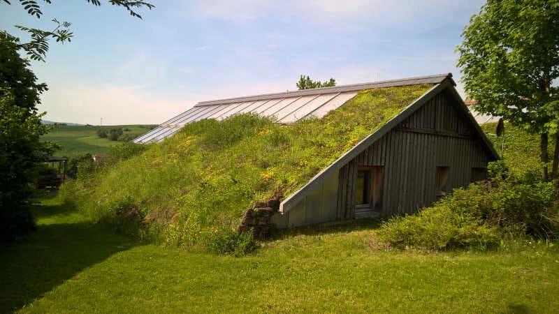 Erdüberdecktes Haus mit begrüntem Schrägdach und großem verglastem Dachband in ländlicher Umgebung.