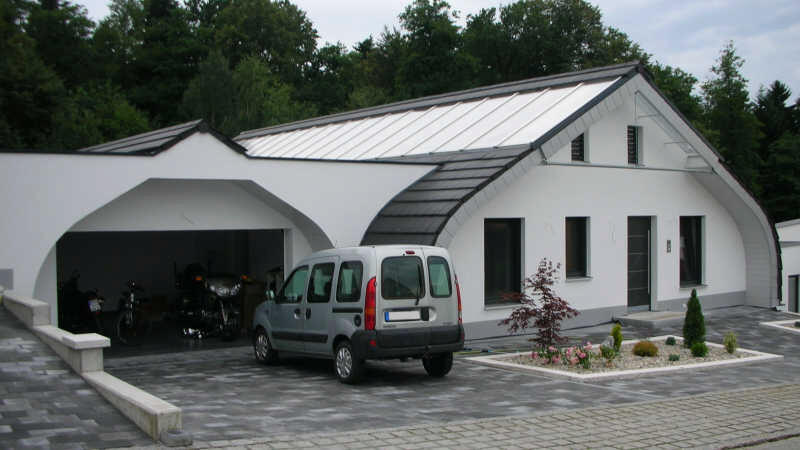 Weißer Bungalow mit Carport, gepflasterter Einfahrt und geparktem Auto, Seitenansicht.