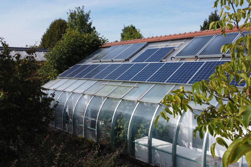 Modernes Solarhaus am Hang mit voll verglaster Südseite, Balkon und großflächiger Photovoltaik auf dem Dach.